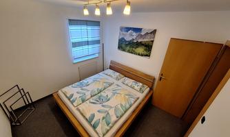 A cozy bedroom with a double bed and colorful bed sheets. A window with blinds and a picture on the wall complete the room.