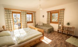 A bright bedroom with two beds and large windows. The rooms are simply and comfortably furnished.