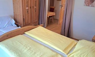 A cozy bedroom with a large bed and yellow bedding. In the background, a wardrobe and a small table can be seen.
