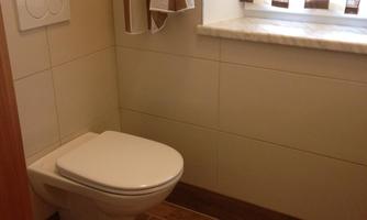 A small bathroom with a white toilet. The window has curtains and there is a small windowsill.