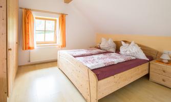 A cozy bedroom with a large double bed and bright wood details. The windows are adorned with orange curtains, bringing plenty of light into the room.