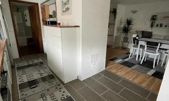 A bright hallway with gray tiles and a decorative rug. In the background, there is a dining area with a table and chairs.