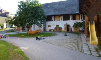 A property with a farmhouse and a large garden. In the foreground, toy vehicles and a slide can be seen.
