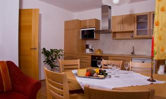 A modern kitchen with wooden cabinets and a dining table. The room is bright and friendly with a cozy red sofa.