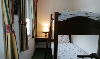 A cozy room with a bunk bed and a warm lamp. The walls are painted light and decorated with curtains.