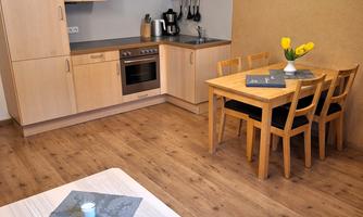 A bright kitchen with wooden cabinets and a dining table. Fresh flowers are in the center of the table, and the rooms feel cozy.