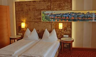 A cozy bedroom with two beds and pillows shaped like lace. On the wall, there is a decorative picture of a city view and soft lighting.