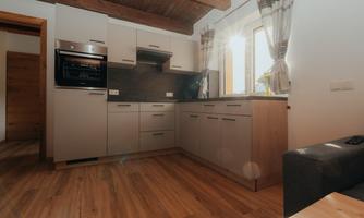A modern kitchen with a wooden ceiling and plenty of natural light. The furniture is in light colors and the floor is made of wood.