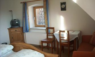 A cozy room with a double bed, a table, and chairs. A window lets in natural light and offers a view of the outside world.