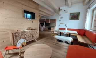 A cozy living space with bright wooden furniture and a modern seating area. A television is mounted on the wall and a colorful picture decorates the room.