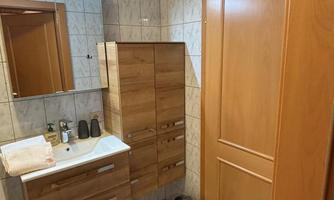A modern bathroom with wooden fittings and bright tiles. The room is well-lit and features a mirror as well as a sink area.