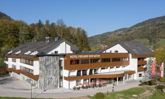 A modern hotel with the sign "Hotel Friends of Nature" in a picturesque landscape.  
Surrounded by green hills and trees.