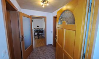 A bright foyer with wooden doors and a modern ceiling light. In the background, a dining area with a table and chairs is visible.