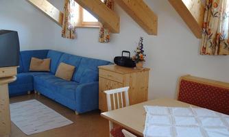 A cozy living space with a blue sofa, a wooden table, and chairs. Large windows allow for plenty of daylight.