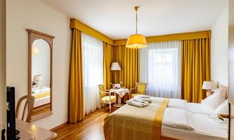 A bright and inviting bedroom with wooden flooring and large windows. The yellow curtains and lampshade create a cozy atmosphere.