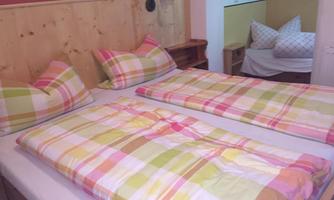 A cozy bedroom with two beds and colorful bed covers. In the background, another bed is visible.