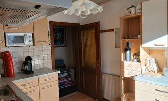 A bright kitchen with modern furniture and wooden flooring. In the background, there is a door leading to another room.