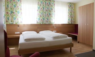 A bright room with a double bed and colorful curtains. There is a desk and a seating area in a cozy atmosphere.