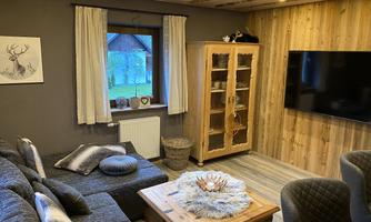 A cozy living room with a gray couch, a wooden table, and a television on the wall.  
Large windows with curtains let in plenty of light, and there is a wooden display cabinet for decoration.
