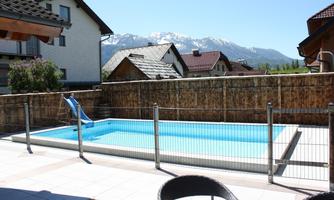 A swimming pool with a slide and a fence surrounding it. In the background, snow-covered mountains are visible.