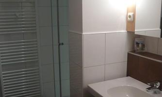 A modern bathroom with a shower and a sink. The walls are light tiled and the lighting is friendly.