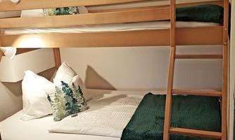 A simple wooden bunk bed in a cozy room. On the beds are cushions and blankets in green and white colors.
