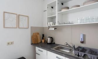 A bright kitchen with white cabinets and a gray countertop. Dishes, glasses, and cooking utensils are visible.