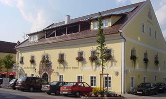 A yellow building with many windows and plants on the walls. In front of the house are several cars and flower beds are laid out.