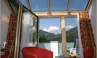 A cozy room with red furniture and large windows. The view shows the mountains and the blue sky.