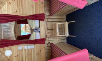 A cozy interior with wooden walls and red curtains. Two beds are facing each other, and a small staircase leads to the seating area.
