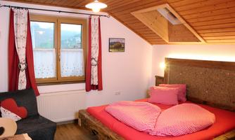 A cozy bedroom with a large heart-shaped bed and wooden decor.  
Windows with curtains and a beautiful view of nature.