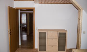 A bright room with a dresser and an open archway. In the background, another room is visible.