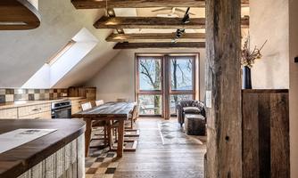A modern kitchen with wooden details and large windows. The room is bright and friendly, with a wooden dining table.