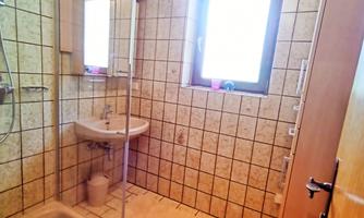 A bright bathroom with a shower and a sink. The floor is tiled and a blue rug is positioned in front of the shower.