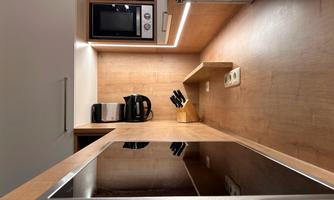 A modern kitchen with wooden surfaces and stylish appliances. The cooking area is well organized with a cooktop, a coffee machine, and a microwave oven.