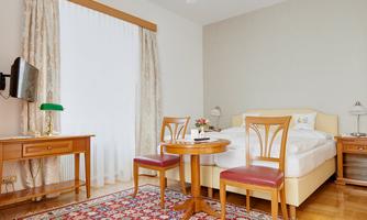 A cozy bedroom with a large bed and a small table. The room has a warm color scheme and plenty of daylight.