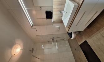A modern bathroom with a large shower and an elegant sink. The walls are brightly tiled, and the furnishings are simple and functional.