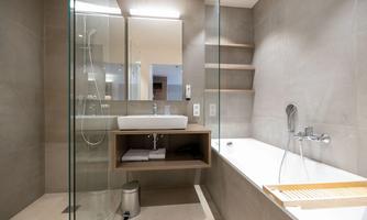 A modern bathroom with a shower and a bathtub. The walls are in neutral gray tones, and there is a wooden shelf.