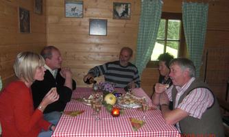 A cozy group of five people is sitting at a table in a wooden cabin. They are enjoying a meal together and chatting.