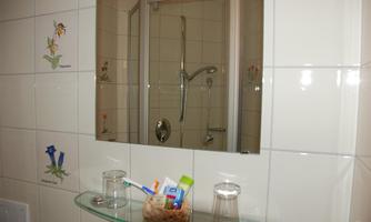 A bright bathroom with a shower behind a glass wall. Some toiletries and glasses are on the sink.