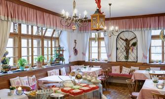 A cozy dining area with wooden decor and large windows. Table decorations and plants create an inviting atmosphere.