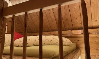 A cozy bedroom in the attic with a wooden bed and natural wood interior. The bedding is bright and cheerful, perfect for a relaxing night's sleep.