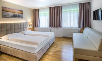 A modern bedroom with a large double bed and a comfortable sofa. Bright windows let in plenty of daylight.