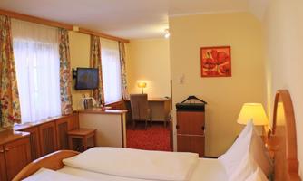 A cozy hotel room with two beds and a desk. The room is warmly decorated and has a window with curtains.