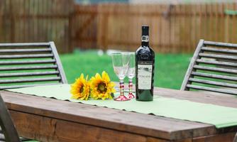 A wooden table outdoors with a bottle of wine, two glasses, and sunflowers. The table is decorated with a green cloth and is located in a garden.