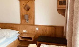 A cozy room with wooden furniture and a bed. On the table is a small flower vase, and the walls are bright.