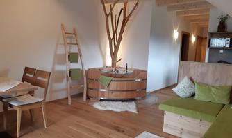 A stylish room with wooden flooring and modern furniture. In the center is a cozy wooden bathtub, surrounded by soft colors and natural elements.