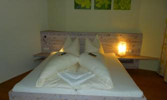 A cozy bedroom with a large double bed and two pillows. In the background, there are green pictures on the wall and soft lighting.