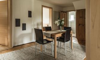 A cozy dining area with a wooden table and black chairs. The room is bright and inviting, with a rug on the floor.