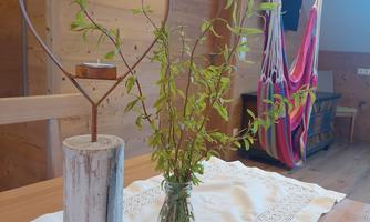 A rustic table with a heart-shaped decoration and a vase with fresh plants. In the background, a colorful hammock is hanging.